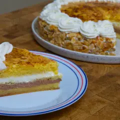 Un trozo de tarta o pastel de capas con crema y almendras, coronado con nata montada.