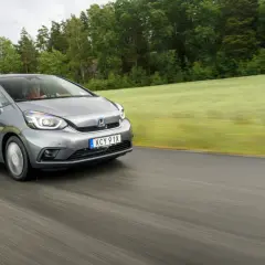 Grå Honda Jazz kör på en väg genom ett grönt landskap. Inga problem med denna bil, bara en härlig tur.