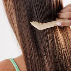 Peinando el pelo largo y castaño, que luce un poco apelmazado, con un peine de madera.