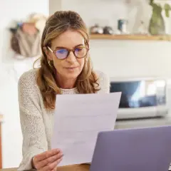 Femme concentrée sur un document, peut-être un modèle lettre déclaration tardive impôts, devant son ordinateur.