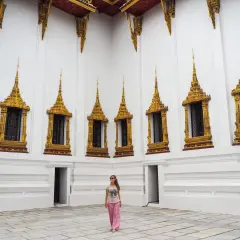 Una mujer sonríe frente a una pared blanca con ventanas doradas ornamentadas, un ejemplo de qué ver en Tailandia.