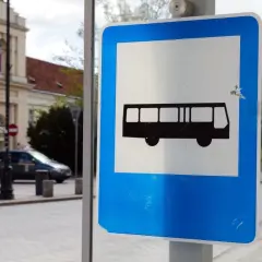 Znak przystanku autobusowego. Czy autobus ma pierwszeństwo? Na ulicy widać samochody i budynek.
