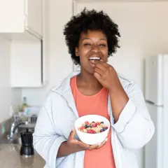 Une femme savoure un bol de céréales et de fruits, un exemple d'alimentation intuitive.