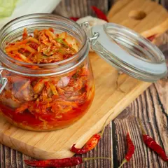 Słoik z domowym kimchi, idealny do przepisów na przetwory domowe. Obok kapusta, czosnek i papryczki chili.