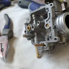 Attrezzi per la pulizia carburatore: pinze e un carburatore smontato, pronto per la manutenzione.