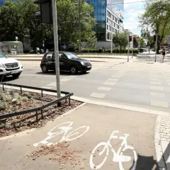 Czarny samochód wyprzedza na pasach, omijając białe auto. Na ścieżce rowerowej widoczne są symbole rowerów.