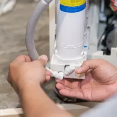 Mains d'un technicien connectant un tuyau à un adoucisseur d'eau, peut-être pour résoudre un problème d'eau salée.