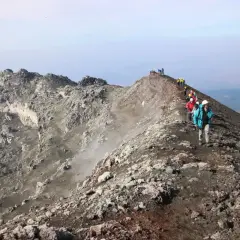 Escursionisti sul sentiero della cima Etna, tra rocce vulcaniche e fumo.