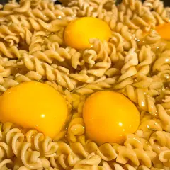 Makaron z jajkiem w trakcie gotowania. Trzy żółtka otoczone przez skręcone nitki makaronu, tworzące apetyczny obraz.