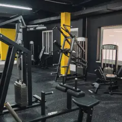 Gym med svarta väggar och gula pelare. Flera träningsmaskiner, inklusive en pec deck, står redo för ett träningspass.
