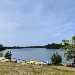 Słoneczny dzień nad jeziorem Chechło. Kolorowe rowerki wodne czekają na plaży, a w oddali widać zalesione brzegi.