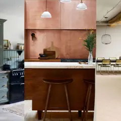 Three distinct kitchens showcase natural wood kitchen design: a sage green hutch, a copper-clad cooking area, and a modern space with exposed beams and a terrazzo island.
