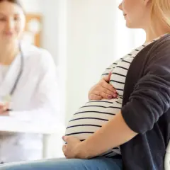 Schwangere Frau im Gespräch mit Ärztin, die den Bauch berührt. Möglicherweise geht es um einen kleinen zuckertest schwangerschaft.