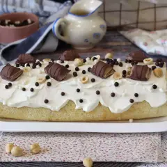 Puszysty biszkopt z kremem, udekorowany kawałkami batoników Kinder Bueno White, orzechami i czekoladowymi kuleczkami.