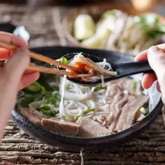 Une cuillère de ce meilleur pho, remplie de nouilles, de viande et d'une touche de sauce piquante, est soulevée avec des baguettes.