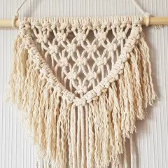Un joli macramé tuto, suspendu à une tige de bois, avec des franges douces et un motif en losanges.
