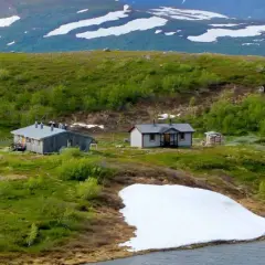 Fjällstugor längs Kungsleden nära Hemavan, med snöfläckar och gröna kullar.
