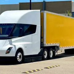 Biała ciężarówka Tesla Semi z żółtą naczepą DHL stoi na parkingu.
