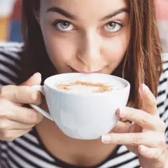 Kobieta z zielonymi oczami pije kawę z mlekiem. Czy od kawy z mlekiem się tyje? To pytanie nurtuje wiele osób.