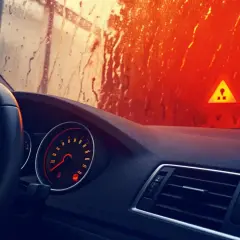 Tableau de bord d'une voiture avec un voyant orange allumé indiquant un système ABS défaillant. Le soleil brille à travers un pare-brise mouillé.