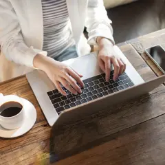 Kobieta pracuje na laptopie, realizując nest bank sesje przychodzące. Obok kawa i telefon.