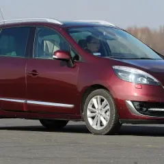 Ciemnoczerwony Renault Scenic 3 z kierowcą za kierownicą jedzie po drodze, w tle drzewa.