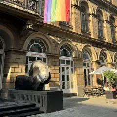 Ein Regenbogenbanner weht über dem von der Heydt Museum. Eine Skulptur steht davor, daneben ein Café mit Sonnenschirmen.