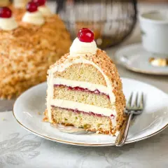 Ein Stück Frankfurter Kranz mit Buttercreme und Kirschfüllung, umhüllt von gehackten Nüssen und garniert mit einer Kirsche.