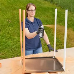 Kvinna sprayar metallbenen på ett bord utomhus. Hon bär skyddsglasögon och handskar.