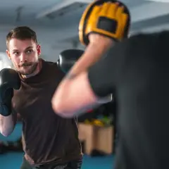 A man in black boxing gloves practices his boxing workout routine, focusing on his opponent holding a yellow mitt.