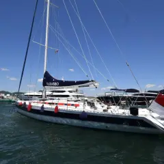 Barca a vela "Nababbo" con bandiera rossa e bianca, in porto con altre imbarcazioni. Sembra una cometa 12.