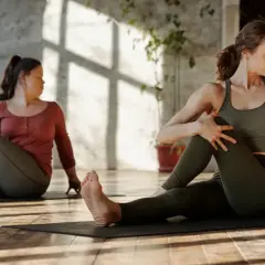 Dwie kobiety wykonują skręt tułowia na macie. To ćwiczenie to właśnie stretching, poprawiający elastyczność.
