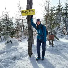 Dziewczyna stoi przy znaku "CZUPEL" w zimowym lesie.