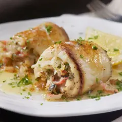 Involtini alla messinese ripieni di pesce e verdure, serviti su un piatto bianco con spicchio di limone e prezzemolo tritato.