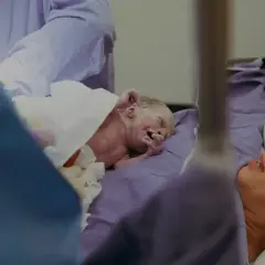Noworodek po indukcji porodu, owinięty w biały ręcznik, leży obok szczęśliwej matki.