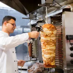 Kucharz w białej kurtce kroi mięso z pionowego rożna na kebab.