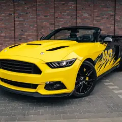 Żółty kabriolet Mustang z czarnymi akcentami i grafiką "1849" na boku. Wygląda jak model z 2026 roku, gotowy na podbój dróg.