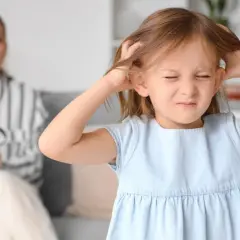 Dziewczynka drapie się po głowie, a kobieta z tyłu trzyma lupę i niebieski przedmiot.