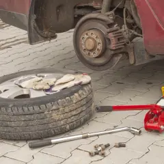 Koło zapasowe, podnośnik, klucz i śruby leżą obok podniesionego samochodu.