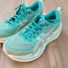 Turkusowe buty do biegania z białym logo, model superblast 2, leżą na drewnianej podłodze.