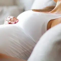 Kobieta w ciąży odpoczywa na kanapie, delikatnie głaszcząc brzuch. Szuka ulgi na mdłości w ciąży, marząc o spokoju.