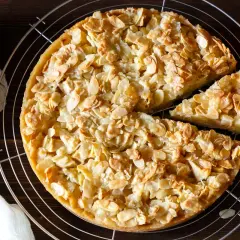 Ein goldbrauner florentiner apfelkuchen mit knusprigen Mandelblättchen, daneben Äpfel und ein Stück Kuchen.