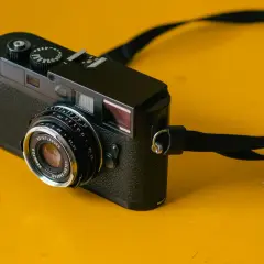 A black camera with a Voigtlander Color Skopar 35mm lens sits on a yellow surface.