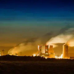 Dymiące kominy elektrowni nocą, ukazujące przyczyny zanieczyszczenia powietrza.