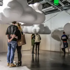 Para szuka inspiracji na warszawskie atrakcje dla dorosłych, pod gigantycznymi chmurami w nowoczesnej przestrzeni.