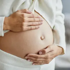 Delikatne ruchy dziecka w brzuchu, kiedy dziecko zaczyna kopać w ciąży. Dłonie matki czule obejmują ciążowy brzuszek.