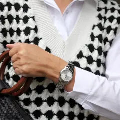 Elegancki zegarek na sztywnej bransolecie, dopełniający stylizację z białą koszulą i kamizelką w czarno-białe wzory.
