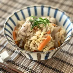 A delicious takikomi gohan recipe served in a striped bowl, featuring rice, chicken, carrots, and green onions.