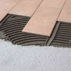 Pose de carrelage droit ou décalé sur lit de mortier frais. Les carreaux beiges sont appliqués sur un support en béton.
