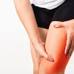 Donna si tiene la coscia, evidenziando un'area rossa che simboleggia l'irrigidimento muscolare delle gambe.